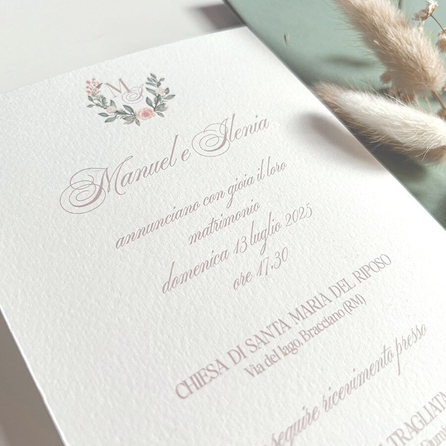 Invito matrimonio romantico con iniziali floreali e scritte eleganti stampato su carta pregiata con dettagli rosa cipria e stile raffinato.