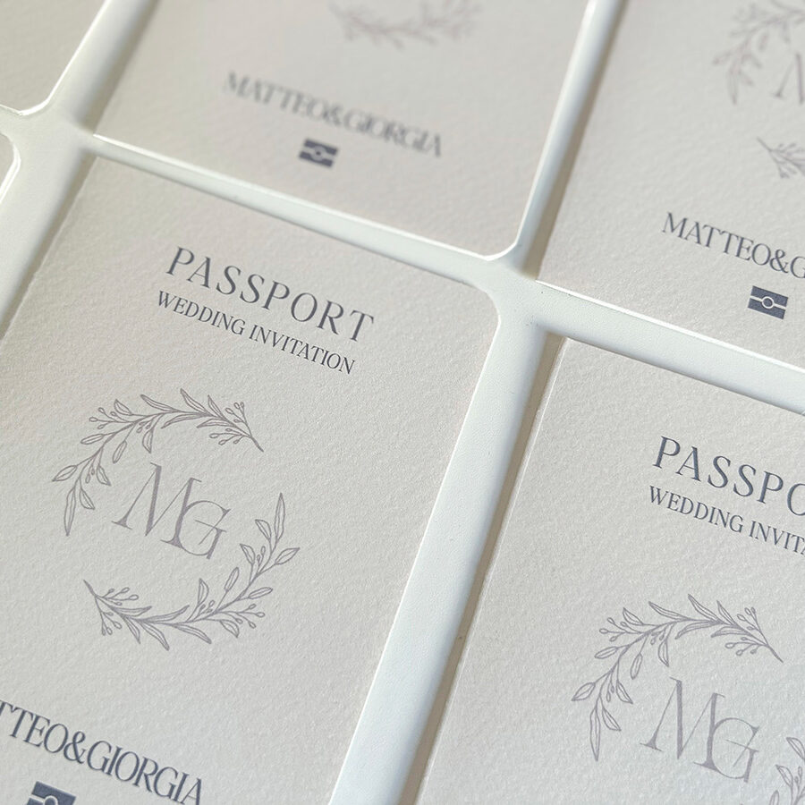 Partecipazioni di matrimonio a tema viaggio con copertina stile passaporto, personalizzate con monogramma e grafica minimal firmate Cupcake Graphics Studio.